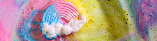 A kids colourful rainbow and cloud bath bomb fizzing away in a bath turning the water into pink and yellow colours.