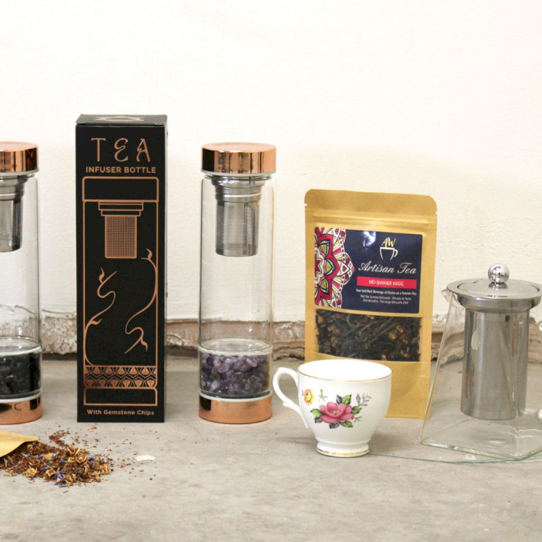 Glass tea infuser bottles displayed with a tea cup, glass tea pot and artisan tea leaves.